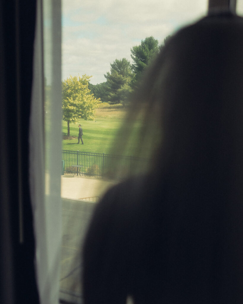 documentary style wedding photos where a bride stands in front of a window looking out to her fiancee before their