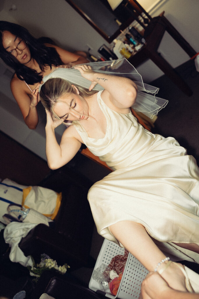 documentary style wedding photos, the bridal party helps the bride into her veil and shoes in this flash photo