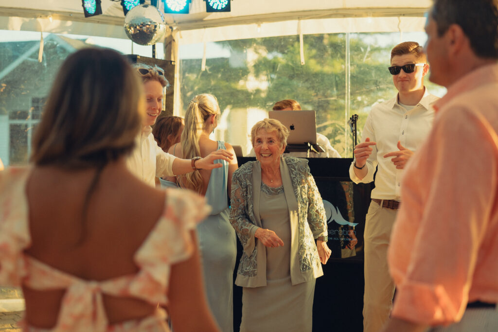 documentary style wedding photos, wedding guests smile as they dance together on the dance floor at a reception