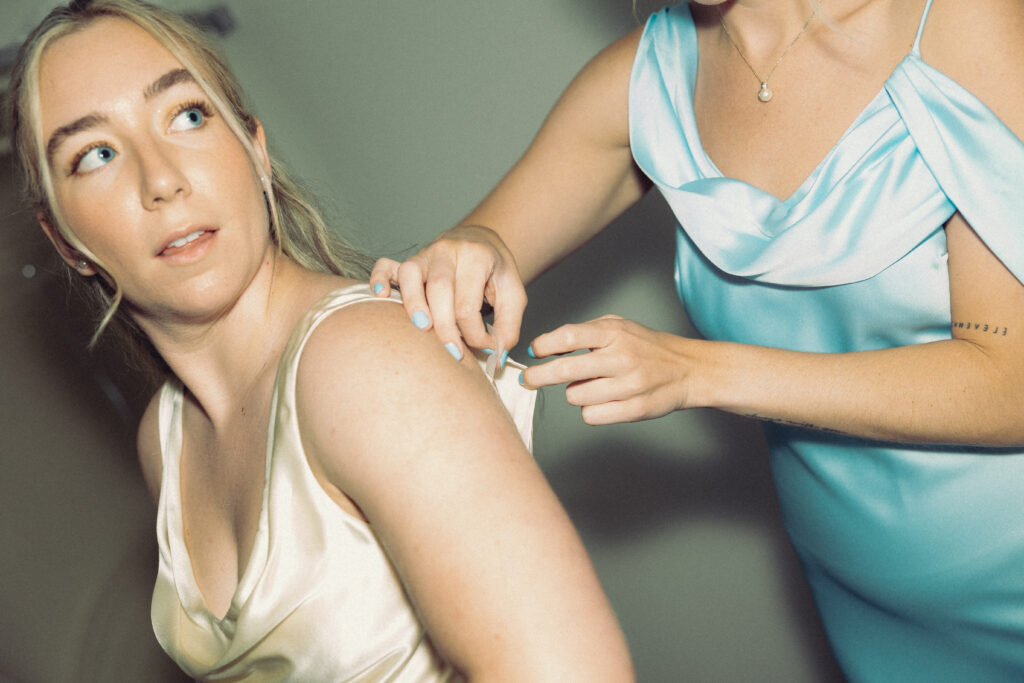 documentary style wedding photos, a bride looks over her shoulder as a bridesmaid helps her into her dress