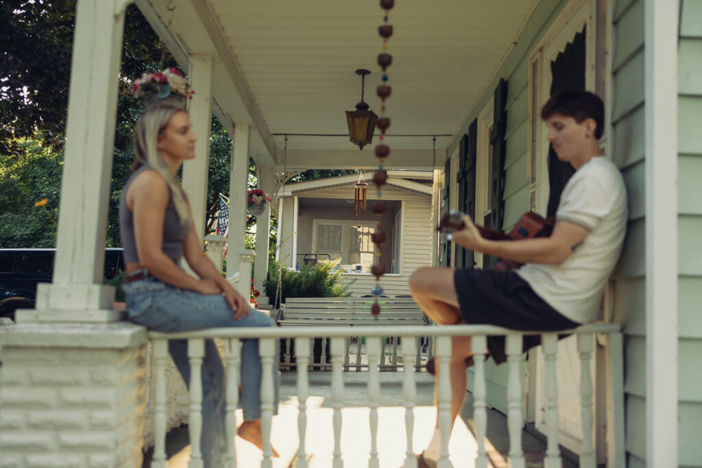 during engagement photos at home a couple sits on the railing of their porch, they are out of focus with the background in focus