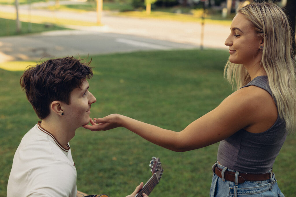 a woman tips her fiancee's face up towards her as he plays guitar for her during their engagement photos