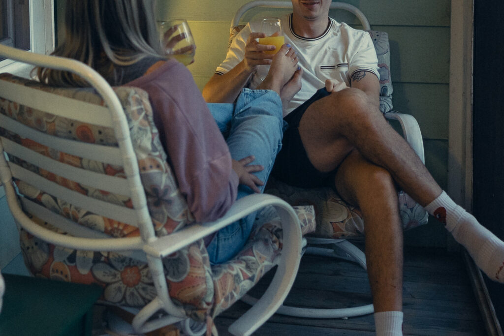  a woman rests her legs in her fiancee's lap as they enjoy mimosas on the front porch during their engagement photos