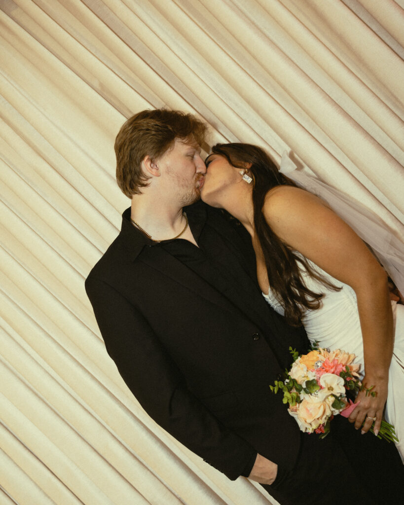newlyweds share a kiss in front of a white pleated curtain for their vegas elopement photography