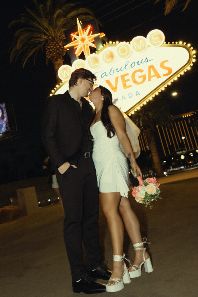 a couple leans in for a kiss in front of the las vegas nevada sign for their vegas elopement photography