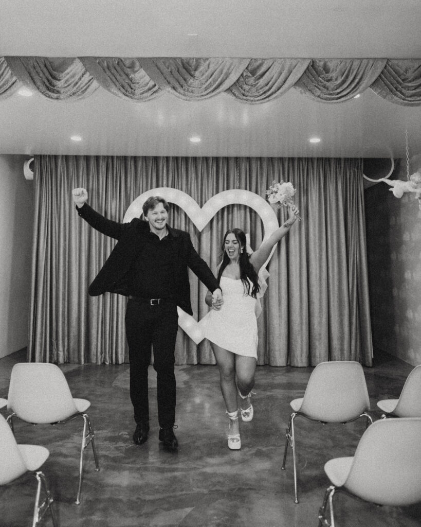 a couple throws their hands in the air smiling during their wedding photos in vegas