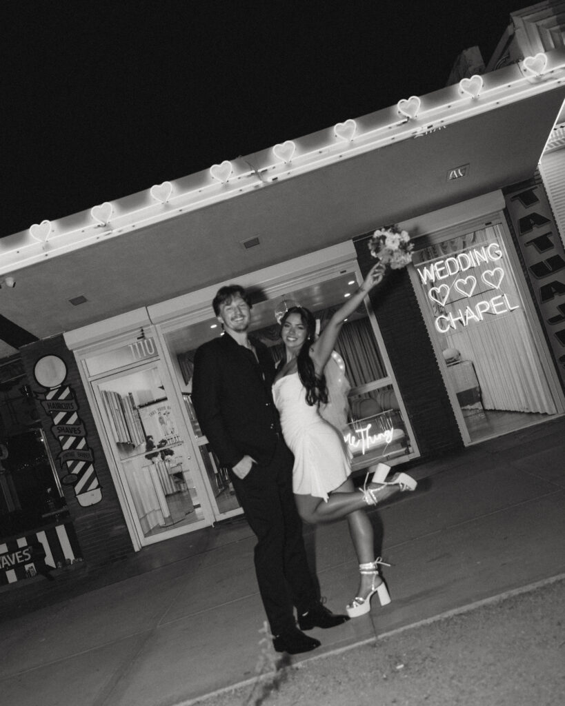 wedding photos in vegas a couple stands in front of the chapel, she raises her arm in the air holding her bouquet