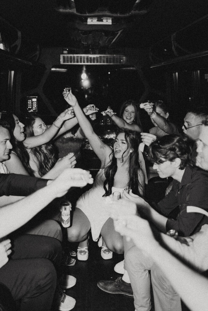 the bride sits in the middle of a party bus with a shot in the air surrounded by her friends for her wedding photographer in vegas