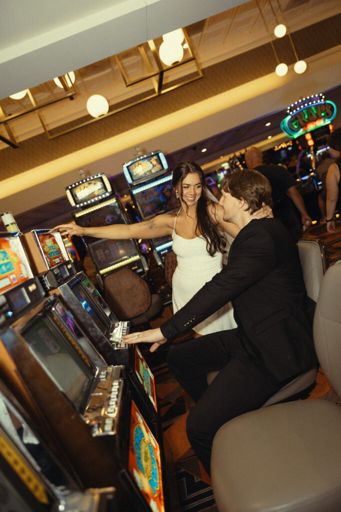 newlyweds smile at each other in front of a slot machine for their wedding photos in vegas