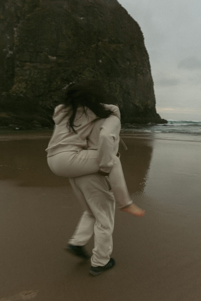 a motion blur portrait of a man giving his wife a piggy back ride on an oregon beach during their elopement photoshoot