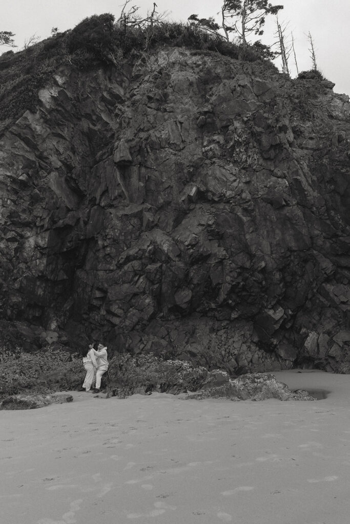 a couple stand together in front of a cliff on the beach 