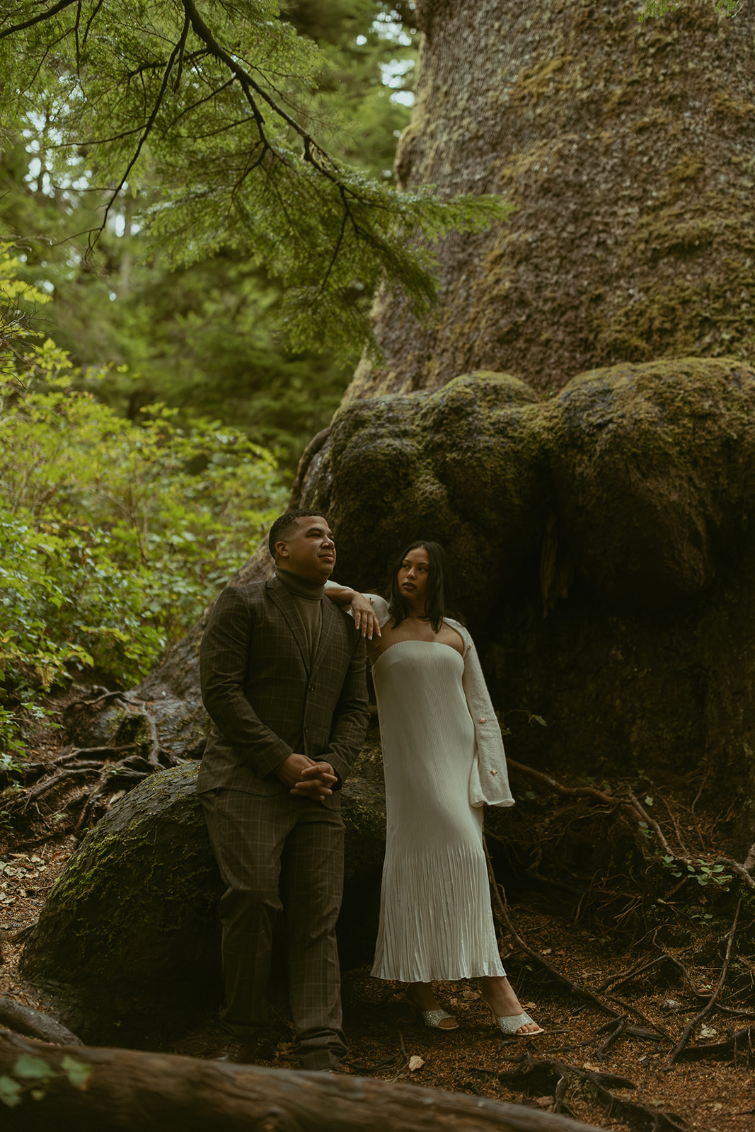 a woman rests her arm on her husband's shoulder while they stand in the forest during their elopement photoshoot