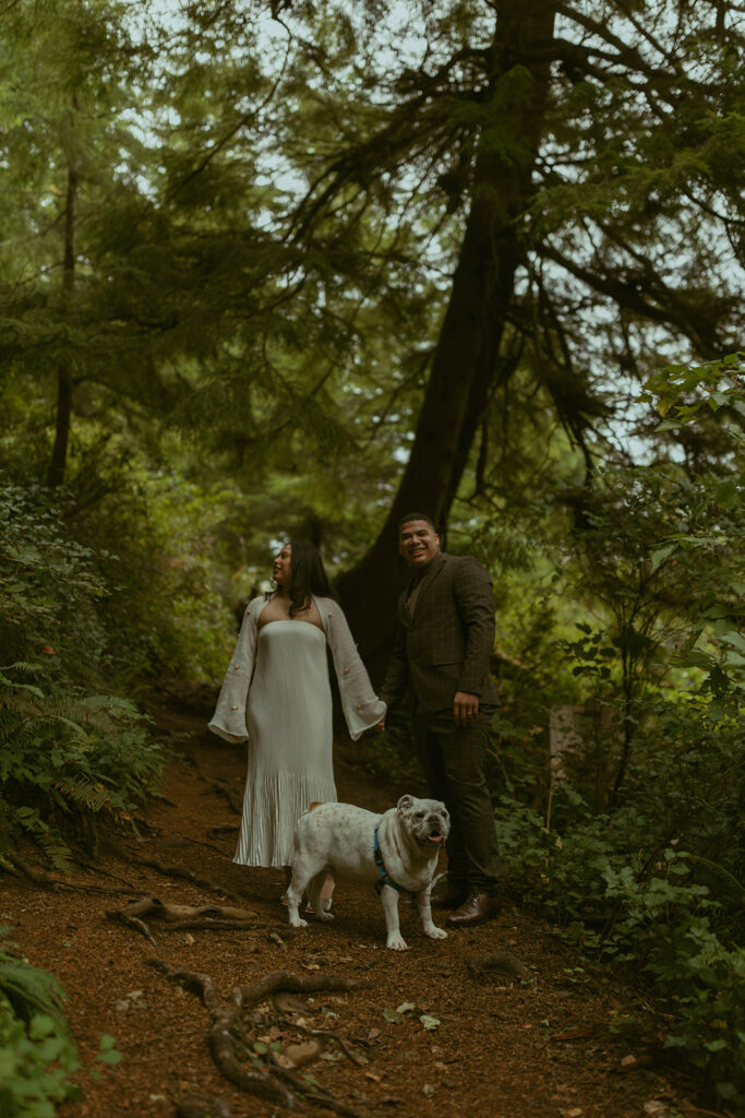 a couple stands in the forest with their dog in front of them during their elopement photoshoot
