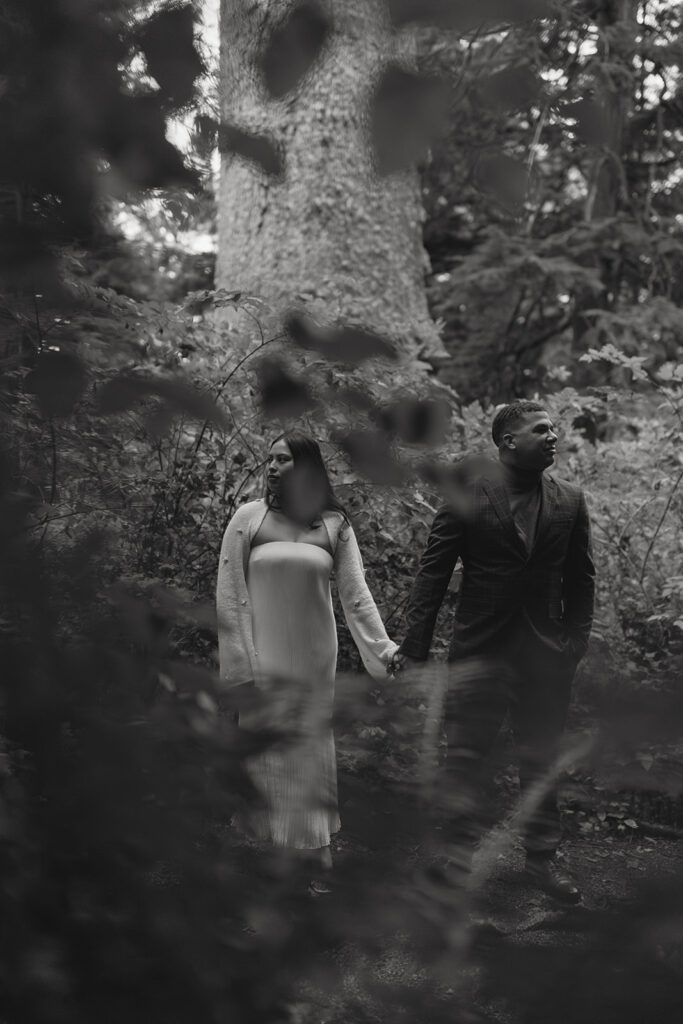 during their elopement photoshoot, a couple stands hand in hand in the forest while looking in opposite direction, framed by foliage