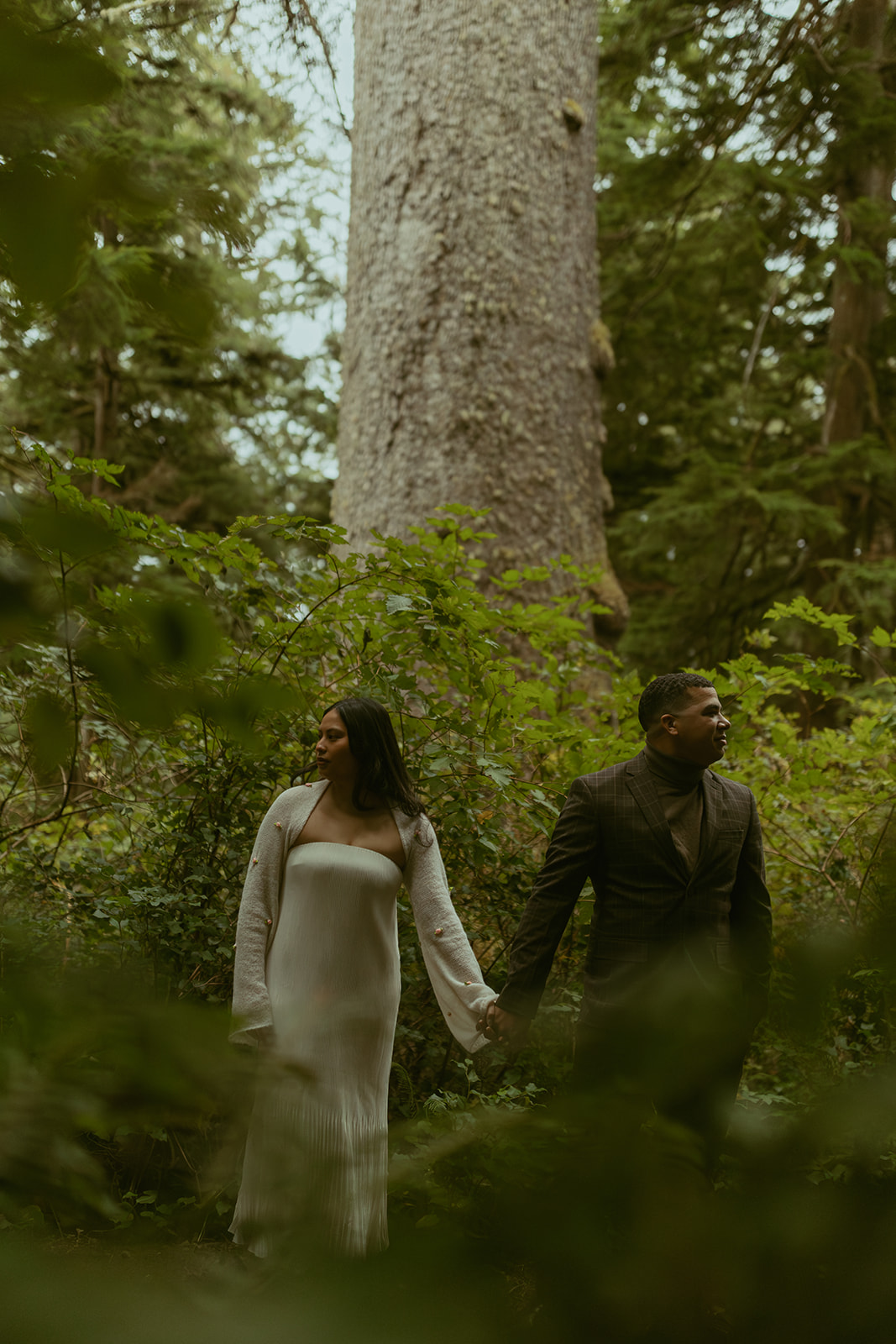 a couple stands in the forest hand in hand framed by foliage with their oregon elopement photographer