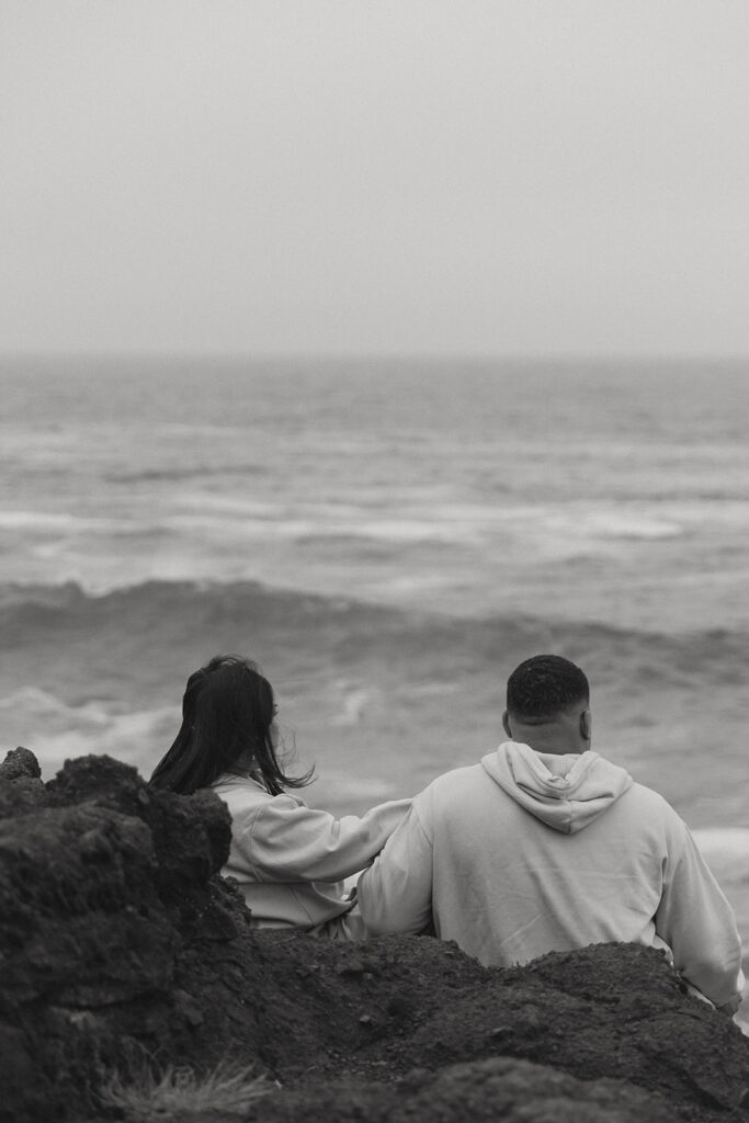 a couple sits next to each other on the rocks in front of the ocean with their oregon elopement photographer behind them