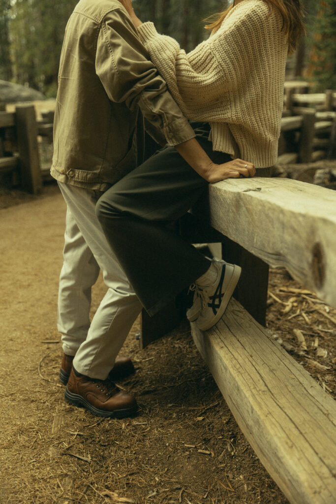 a cropped photo of a couple in an embrace as she sits on a wooden railing at sequoia national park