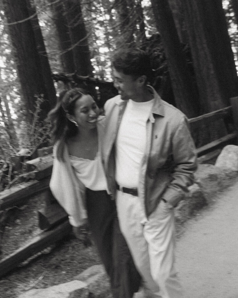 a black and white motion blur portrait from sequoia national park engagement photos where the couple smiles while walking together, her tucked under his arm