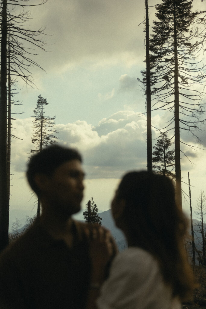 sequoia national park engagement photos of an out of focus couple with a blue sky and clouds, trees, and mountains in the background