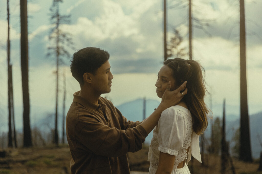 sequoia national park engagement photos where a man looks at his fiancee with his hands on her face as she smiles at him with trees and mountains behind them