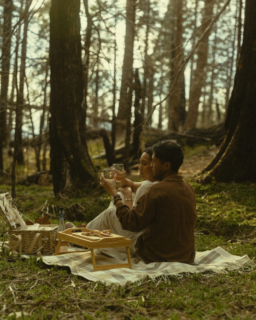 sequoia national park engagement photos where a couple sit together and clink their glasses while sharing a picnic on a blanket on the ground