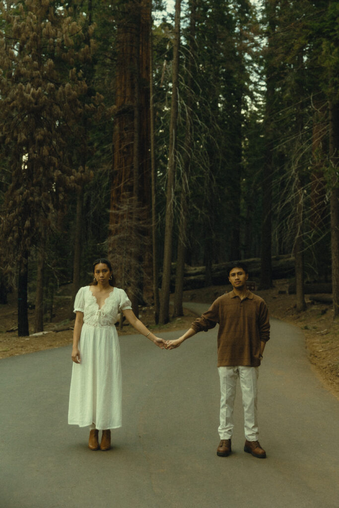 sequoia national park engagement photos where the couple stand around a yard apart on a paved road and hold hands while looking at the viewer