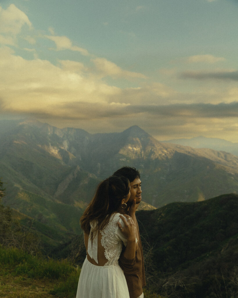 a woman presses a kiss to her fiancee's cheek while they stand in front of a majestic view