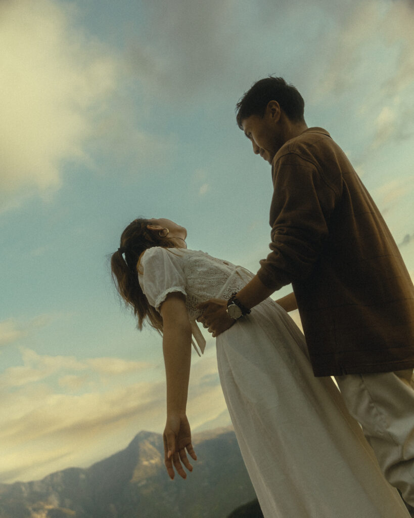 sequoia national park engagement photos where the couple stand in front of the mountains and soft sky, he holds her waist as she leans back and looks to the sky