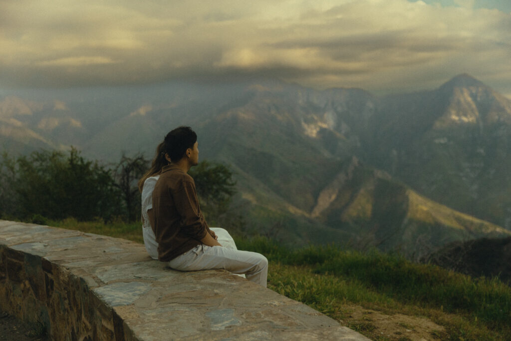a couple sits on a stone bench in front of sprawling mountain view