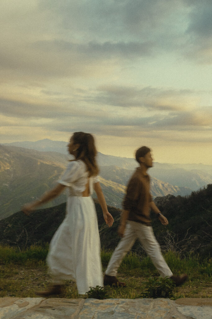 a motion blur portrait of a couple walking in opposite directions during their sequoia national park engagement photos in front of a view of the mountains and a soft sky