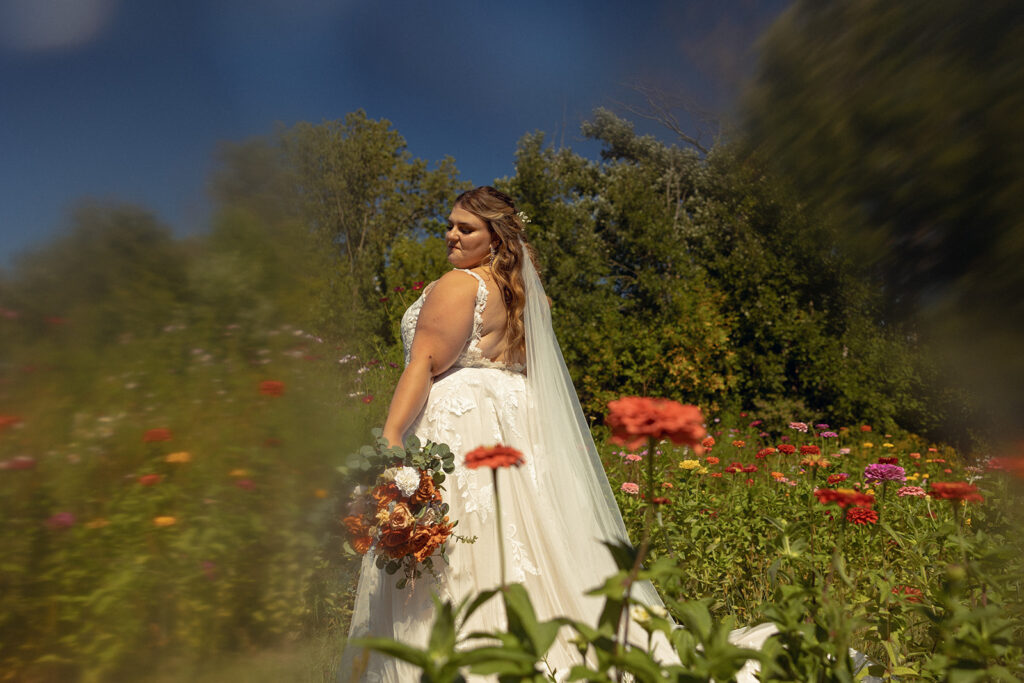 A Michigan bride in a lace bridal gown stands in a field of coral flowers at one of many wedding venues in grand rapids 