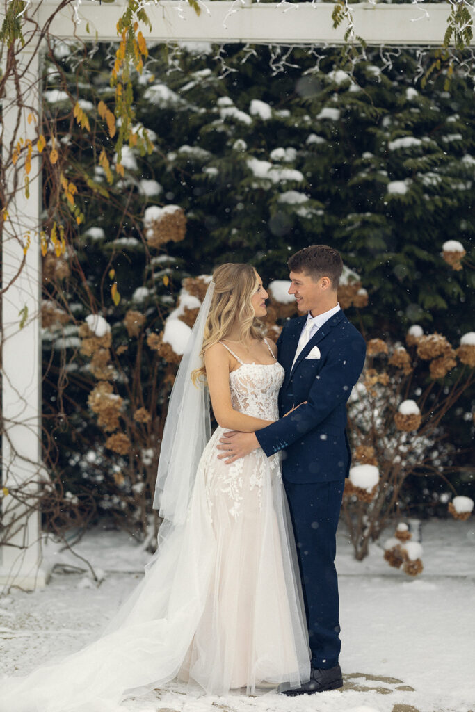 A Michigan bride & groom are pictured surrounded by snow covered shrubs at their winter wedding at one of the hotel wedding venues grand rapids