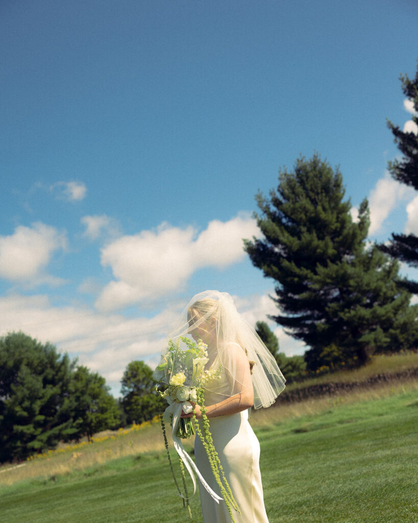 A bride clutches her bouquet and stands against a blue sky at an outdoor wedding venue in grand rapids michigan