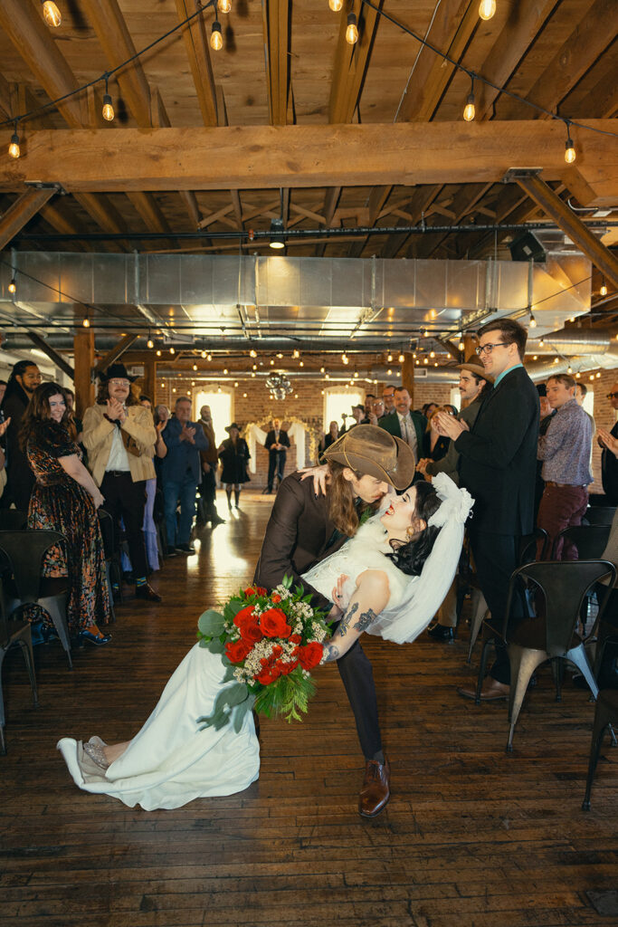 A cinematic photo of a groom dipping his bride for a kiss at the end of the aisle at their Battle Creek, MI wedding 