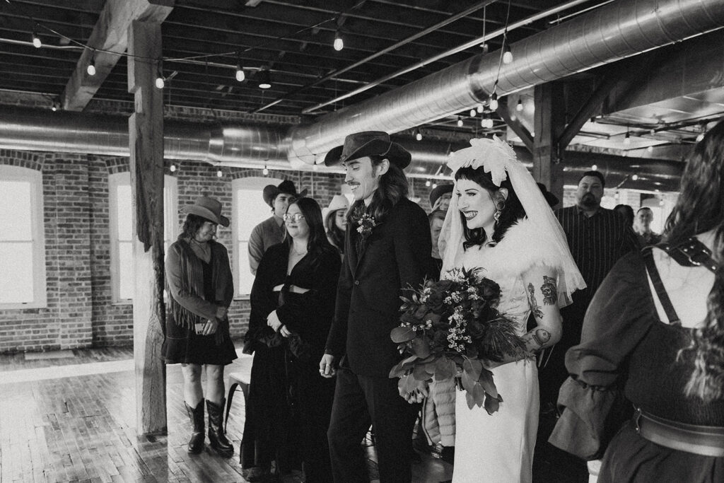 A black and white image of a bride and groom smiling on their way to the altar at their Southwestern Michigan wedding 