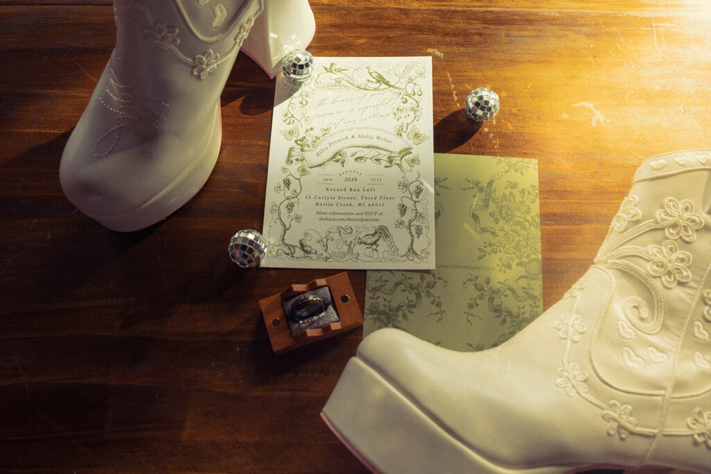Detail shot of white platform cowboy boots, disco balls, and a wedding invite for a '70s aesthetic intimate wedding michigan