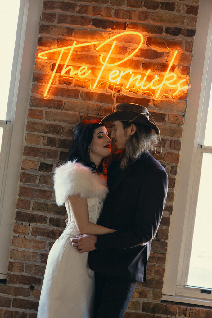 A Michigan couple embraces beneath a neon sign featuring their last name at their Battle Creek wedding at Record Box Loft