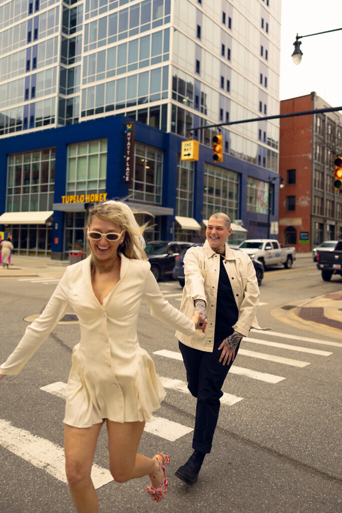 A couple laughs as they run hand-in-hand across the street in Grand Rapids MI before their michigan courthouse wedding