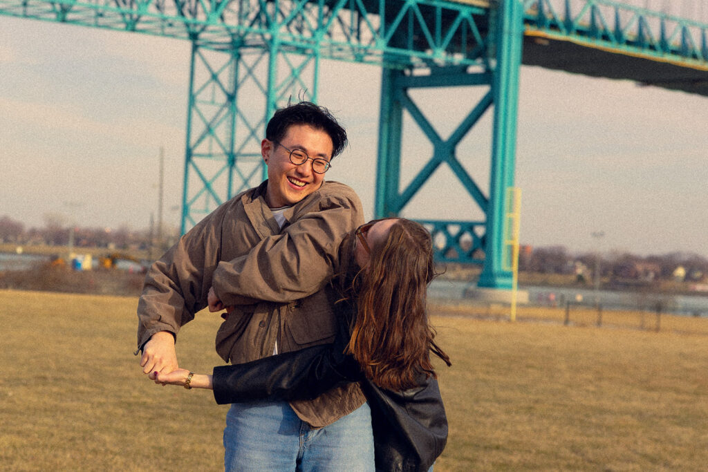A Michigan couple laugh near the River Walk during their Detroit engagement photos 
