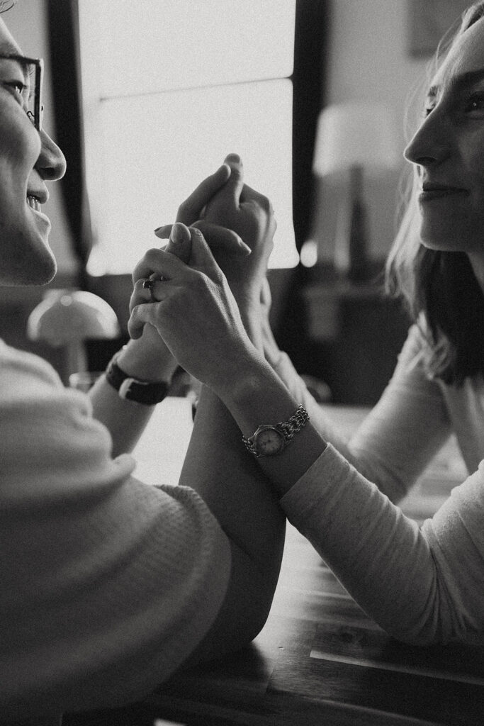 A b+w image of a couple holding hands at a table at Vespers Books and Wine, one of the Detroit engagement photo locations during their shoot