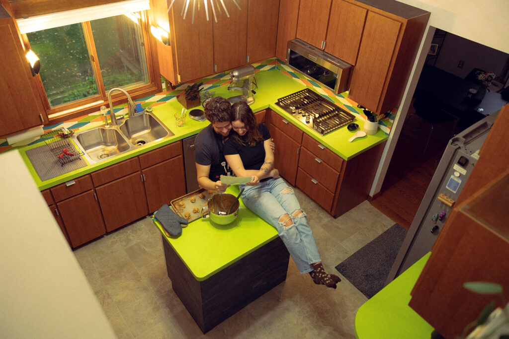A newly engaged couple is photographed from above on seated on their kitchen counter during a lifestyle engagement session in their vintage house in michigan