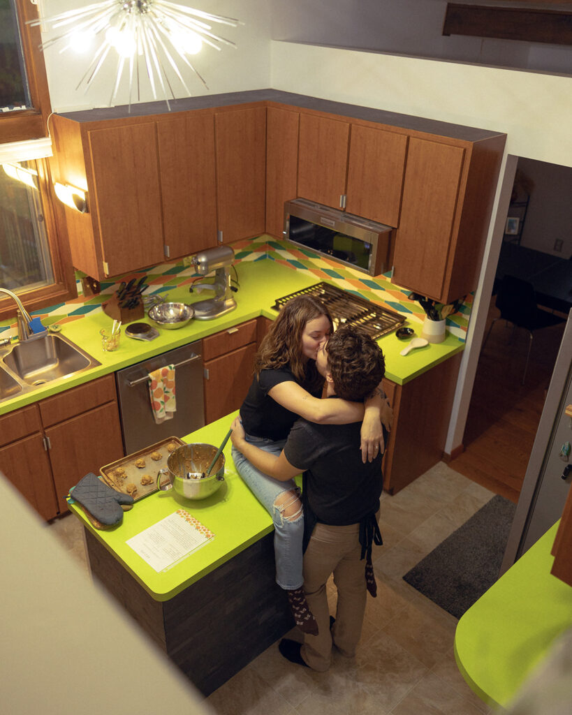 A MI couple shares a kiss in the kitchen of their home during in-hom michigan engagement photos