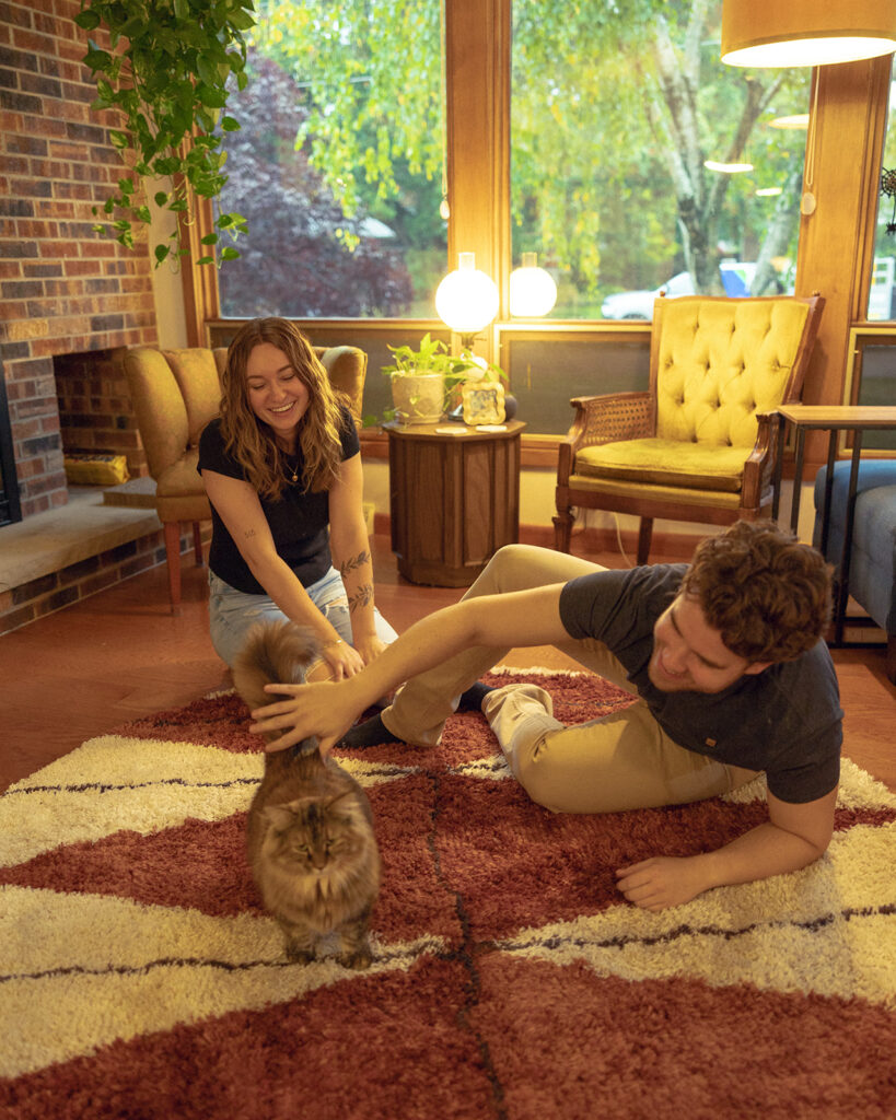 A young couple relax on the rug of their MCM living room during their Michigan engagement photos 