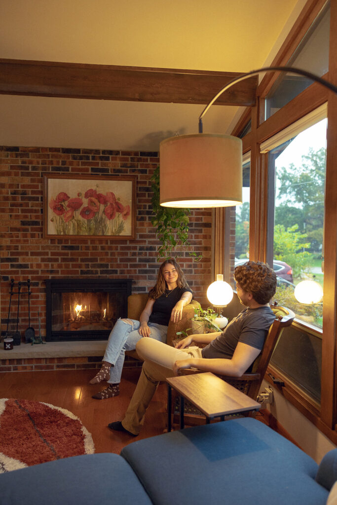 A Michigan couple relax next to their brick fireplace in their MCM home during their Michigan engagement photos 