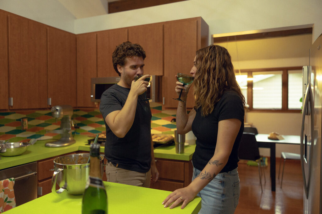 A Michigan couple share a drink in their MCM kitchen during grand rapids engagement photos