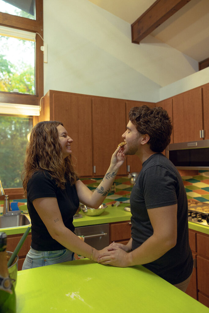 A Michigan woman shares a fresh baked chocolate chip cookie with her fiance during an in-home session shot by engagement photographers grand rapids mi