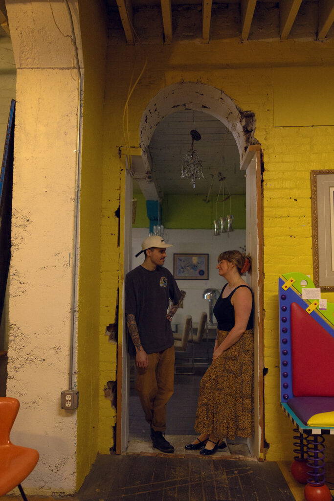 A Michigan couple stand beneath a yellow arch in Lost & Found, a local antique store, during their Michigan engagement photos