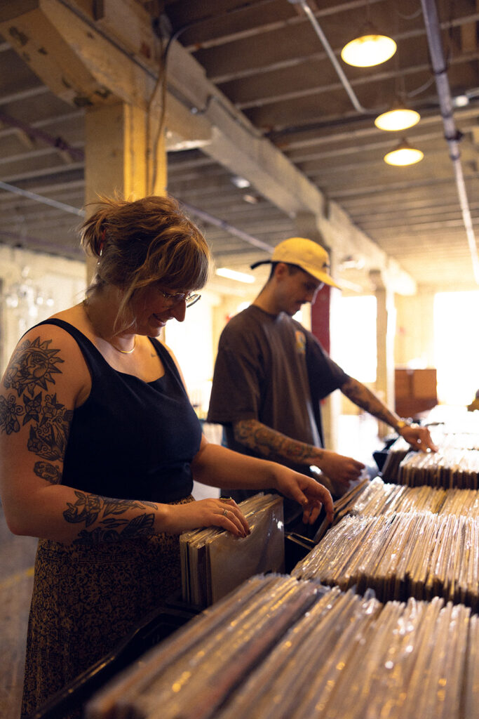 A couple browse the vinyl album stacks at Lost & Found, a local antique store, during a storytelling engagement session with a West Michigan photographer