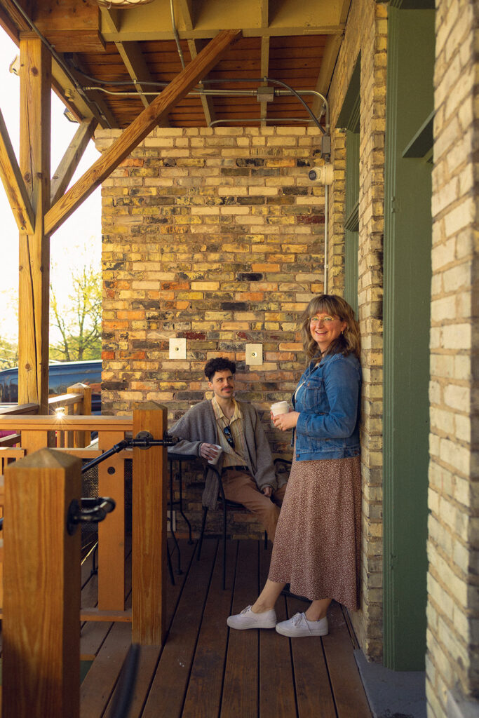 A couple enjoy coffee outside Lyon Street Cafe during engagement photos with a West Michigan photographer