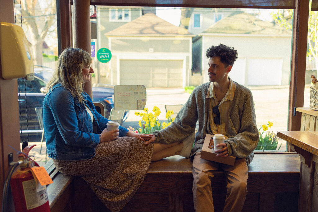 A MI couple are seated in a window of a Grand Rapids coffee shop during a storytelling engagement session with West Michigan photographer, Anika B Photography